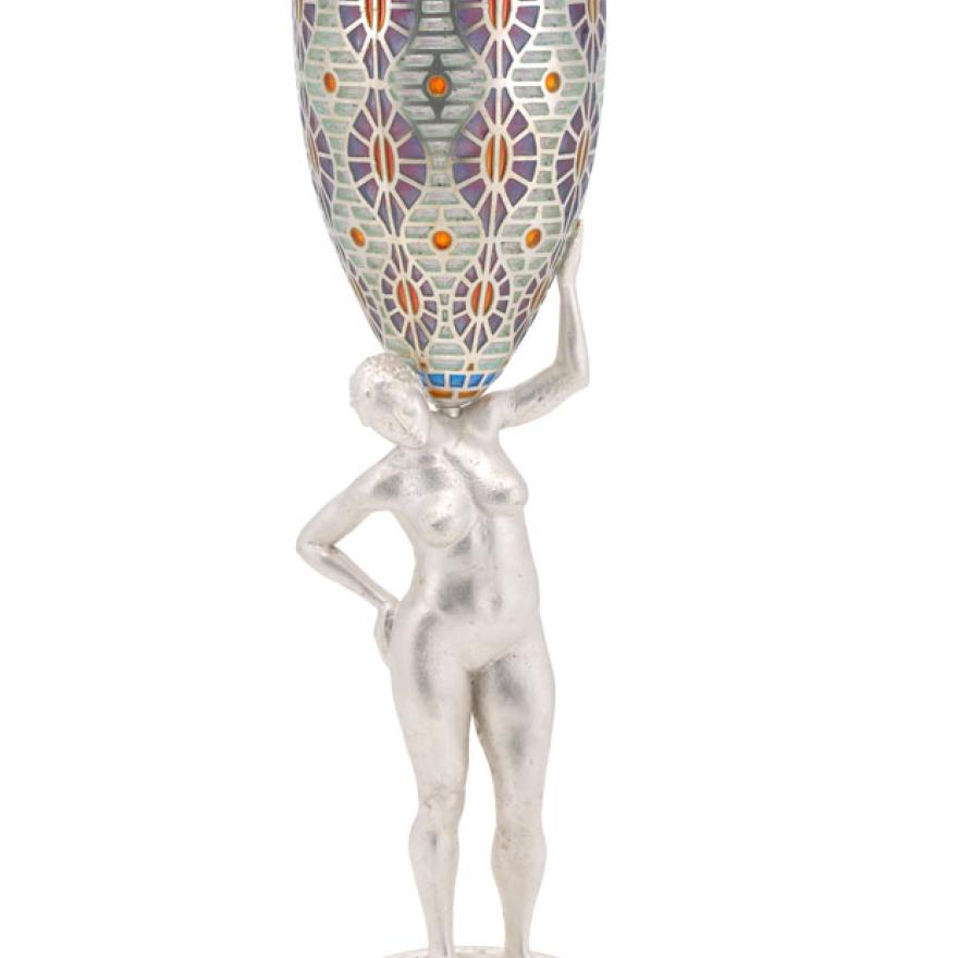 Um copo de vinho alto com um padrão pintado colorido no vidro. A haste do copo é uma estatueta de prata de uma mulher nua