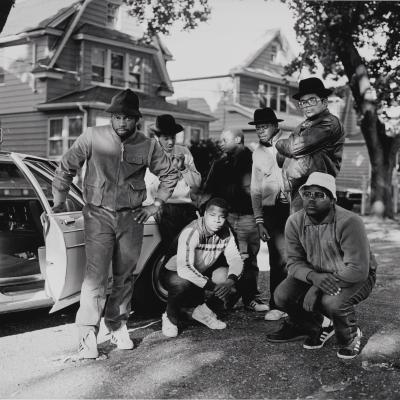 RUN DMC com um grupo de homens posando ao lado de um carro em Hollis, Queens.