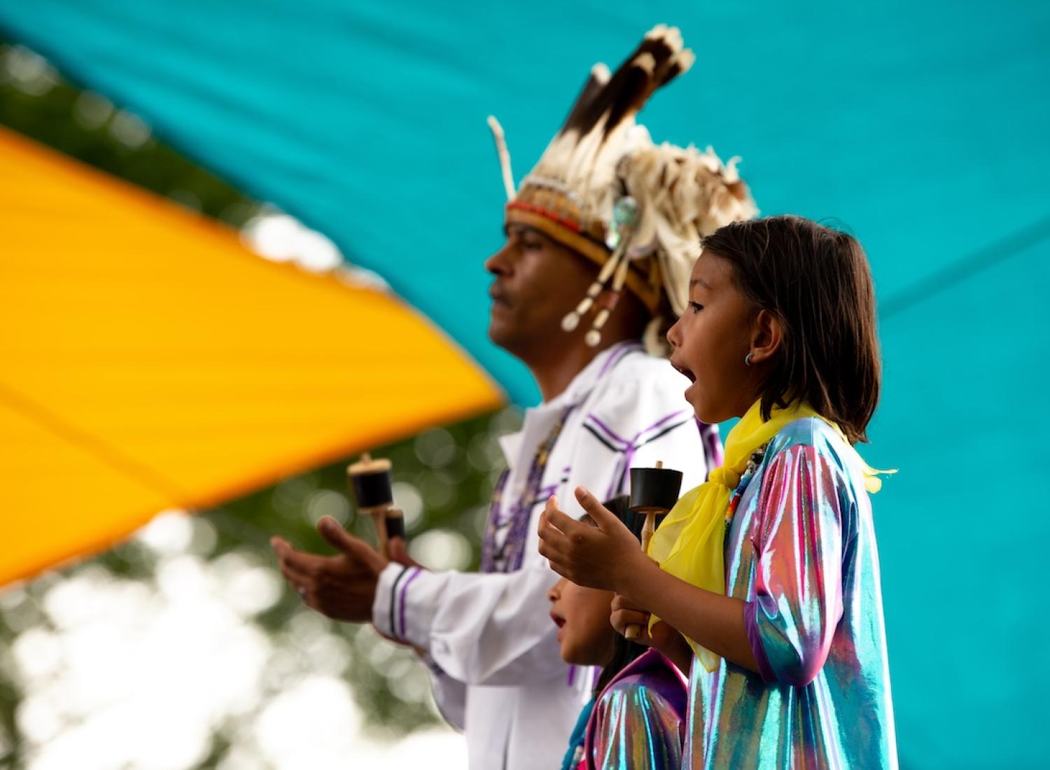 전통 의상을 입은 남자와 어린 소녀가 청록색 배경 앞에서 노래를 부르고 있습니다.