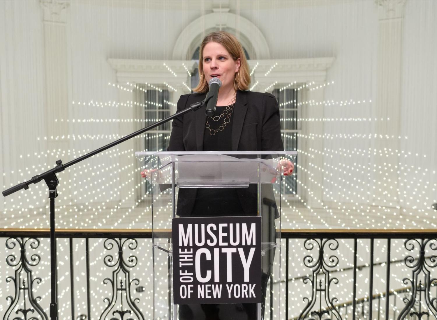 Image of curator Lilly Tuttle at clear podium with text logo "Museum of the City of New York"