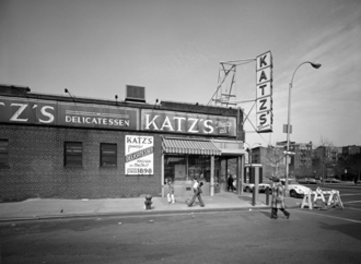 Vista exterior de Katz's Delicatessen en la intersección de las calles Ludlow y Houston con algunas personas caminando.