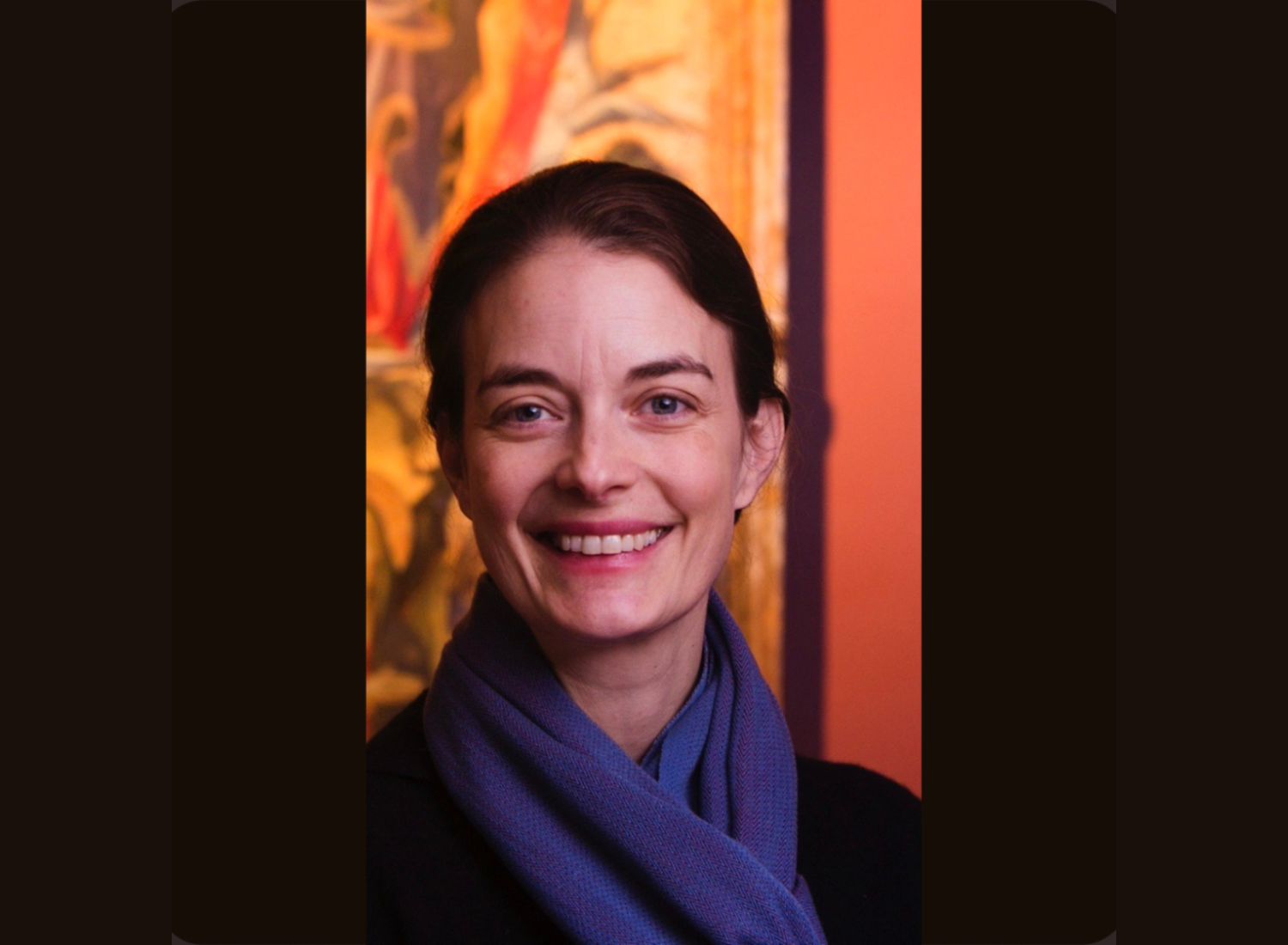 Woman in a purple scarf smiling in front of an orange background
