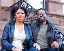 Cynthia Gordy-Giwa e Tayo Giwa, um casal negro, estão sentados nos degraus de um prédio de arenito, vestindo jaquetas de couro e olhando para a câmera.