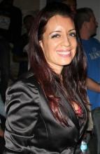 Rebecca Lynn smiles in 3/4s view into the camera. She wears a black satin blazer.