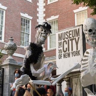 두 개의 큰 해골 인형이 서로 마주보고 있습니다. 그 뒤에 "뉴욕시립박물관"이라고 적힌 푯말이 있다.