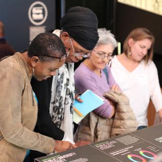 Four women observe a display in a gallery. 