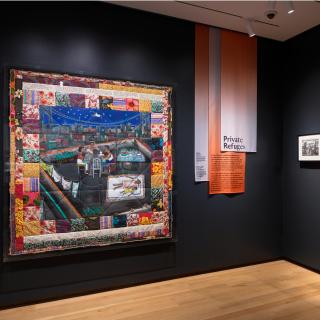 A large colorful quilt hangs on the wall of a gallery.