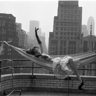 Woman laying in a hammock on a roof with the city skyline in the background 