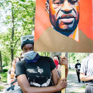 A person in a mask holds up a sign.