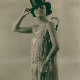 Una fotografía en blanco y negro de Florence Mills posada en un elegante vestido con sombrero de copa y bastón