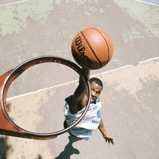 View from above a basketball hoop without a net, where a player is seen about to dunk a basketball through the hoop