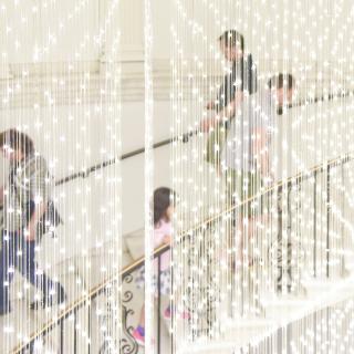 A crowd ascends a spiral staircase behind a light installation