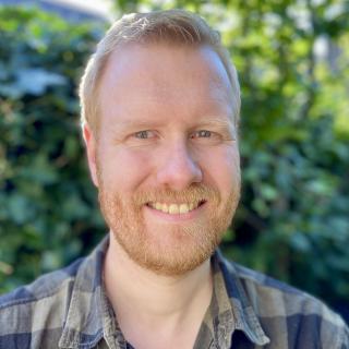 A man in a plaid shirt smile at the camera. 