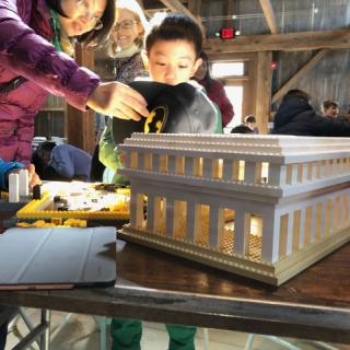 Picture of family of mother, boy, and child with an onlooker behind looking in awe at a LEGO construction