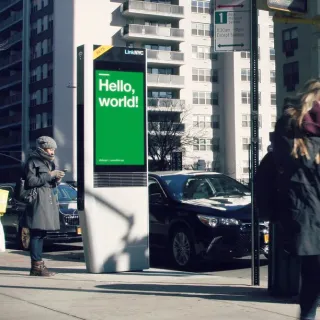 People walk down the street in front of a LinkNYC screen.