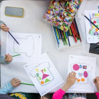 Three children creating an artwork with colored pencils and cut paper.