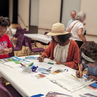 Three people draw at a table. 