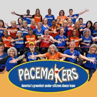 Image of a group of adults wearing blue and orange tshirts with arms open wide smiling at the camera behind a logo that reads Pacemakers