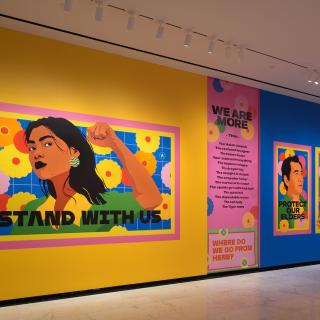 Installation shot of "Raise Your Voice," showing vibrant, colorful drawings of individuals with text.