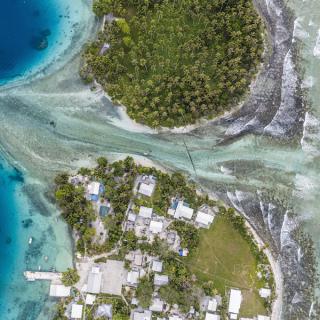 Ejit Island as seen from above. The ocean cuts through two lush green landmasses—with structures visible on the one towards the bottom of the image, and enters into a deep blue patch of ocean. 