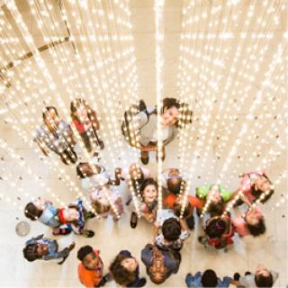 Image looking down on a group of students standing underneath a cascade of small lights. 