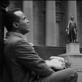 A back and white still of the movie. Harry Belafonte sits leaning on a lampost in a deserted New York.