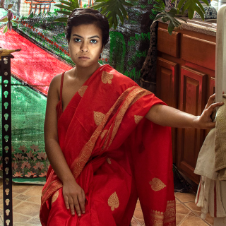열린 냉장고 문에 손을 얹고 빨간 드레스를 입고 부엌 의자에 앉아 있는 여성의 이미지.