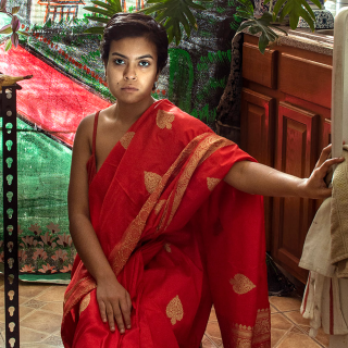 Image of Women sitting on a chair in a kitchen wearing a red dress with their hand on an open refrigerator door.