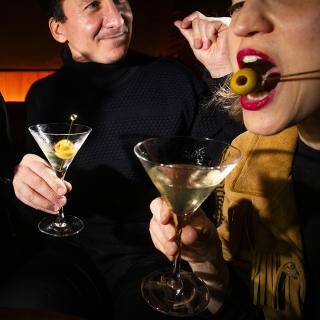 Two people drinking martinis with olives