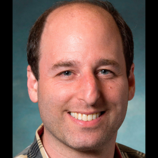 A close up of a man smiling behind a blue background
