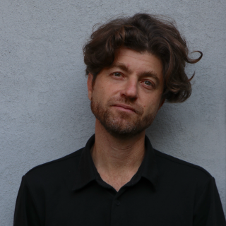 A man smiling in front of a grey wall