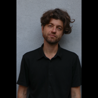 A man smiling in front of a grey wall