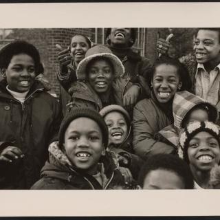 A group of children gather together and smile at the camera. 