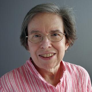 A woman in glasses and a pink shirt smiles at the camera. 