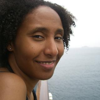 Close-up headshot of a smiling woman on a boat facing the camera with open water and small slivers of land in the background.